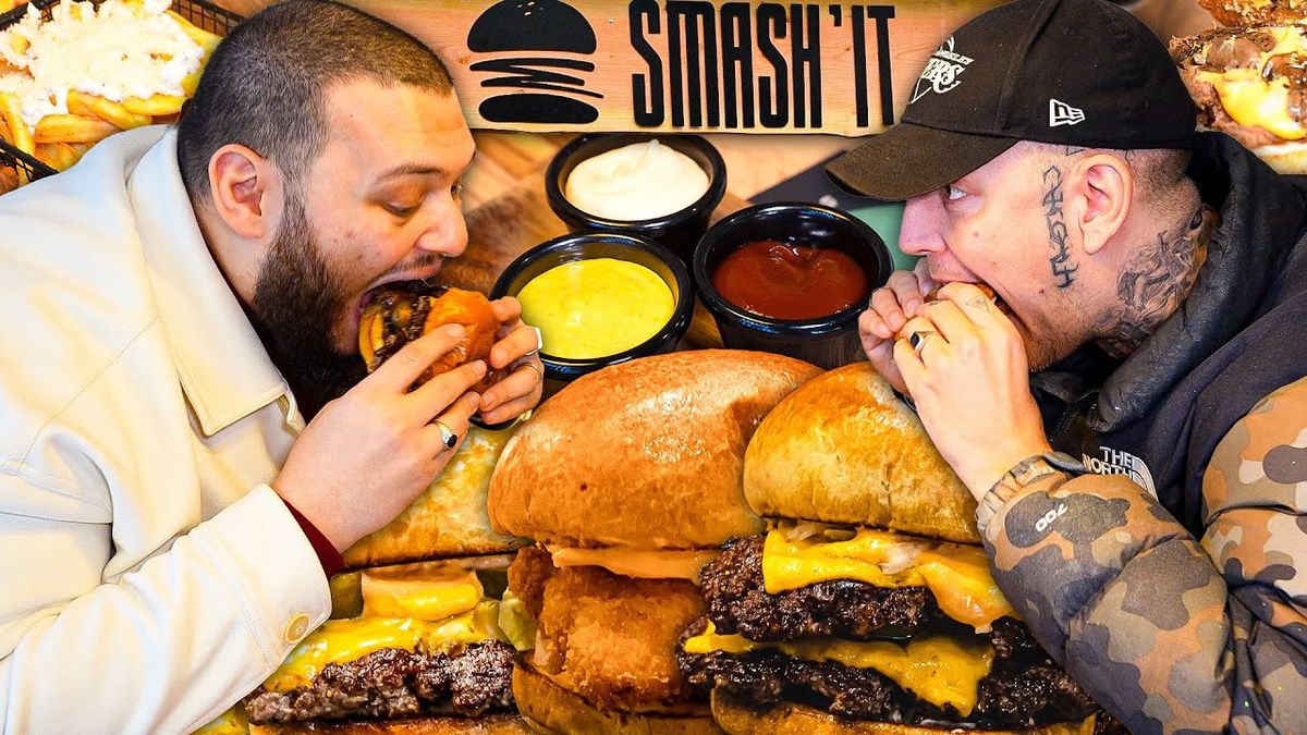 Alt-Text: "Video-Thumbnail von AbuGokus Video 'MONTE ZEIGT MIR DEN BESTEN BURGER IN BUXTEHUDE'. Das Bild zeigt AbuGoku und Monte vor einem Burger-Restaurant in Buxtehude, beide lächelnd und mit einem Burger in der Hand. Der Hintergrund zeigt das Restaurant-Schild und einige Passanten, die vorbeigehen.